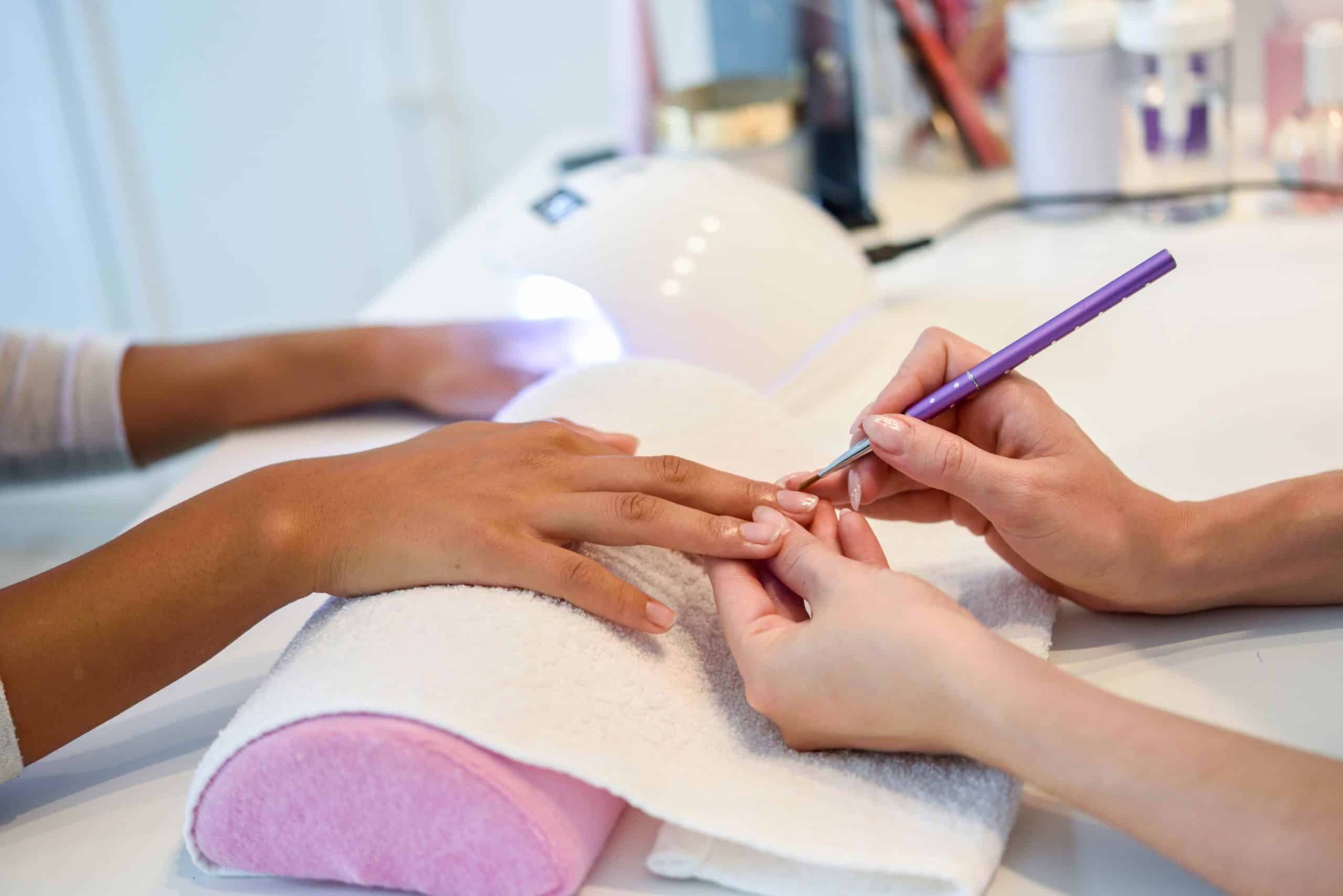 Imagem em foco de uma manicure fazendo a unha de uma cliente